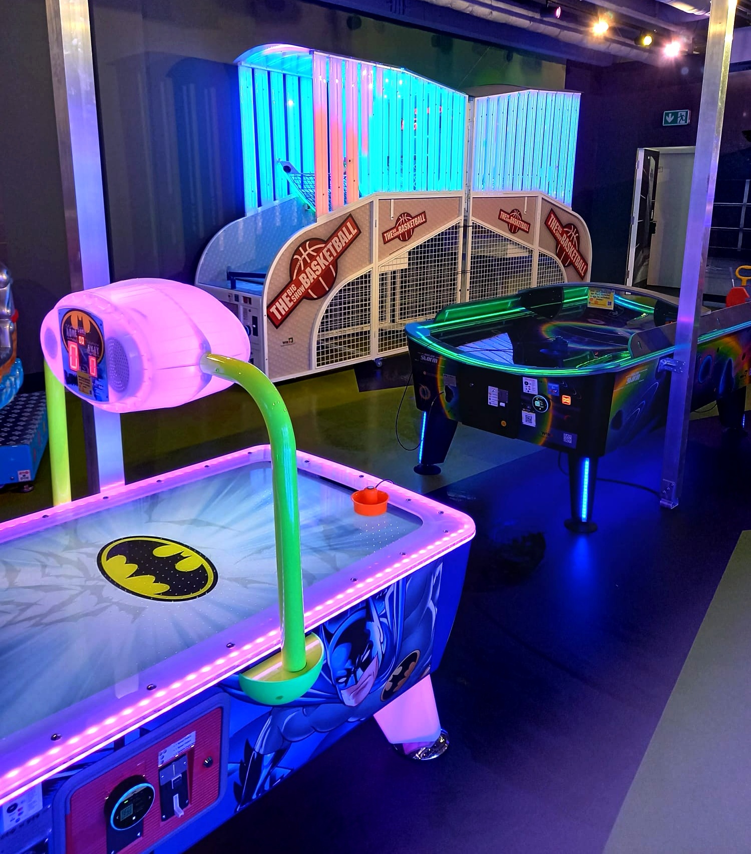 Batman Air-Hockey-Tisch und Basketball-Automat unter bunten Neon-Röhren